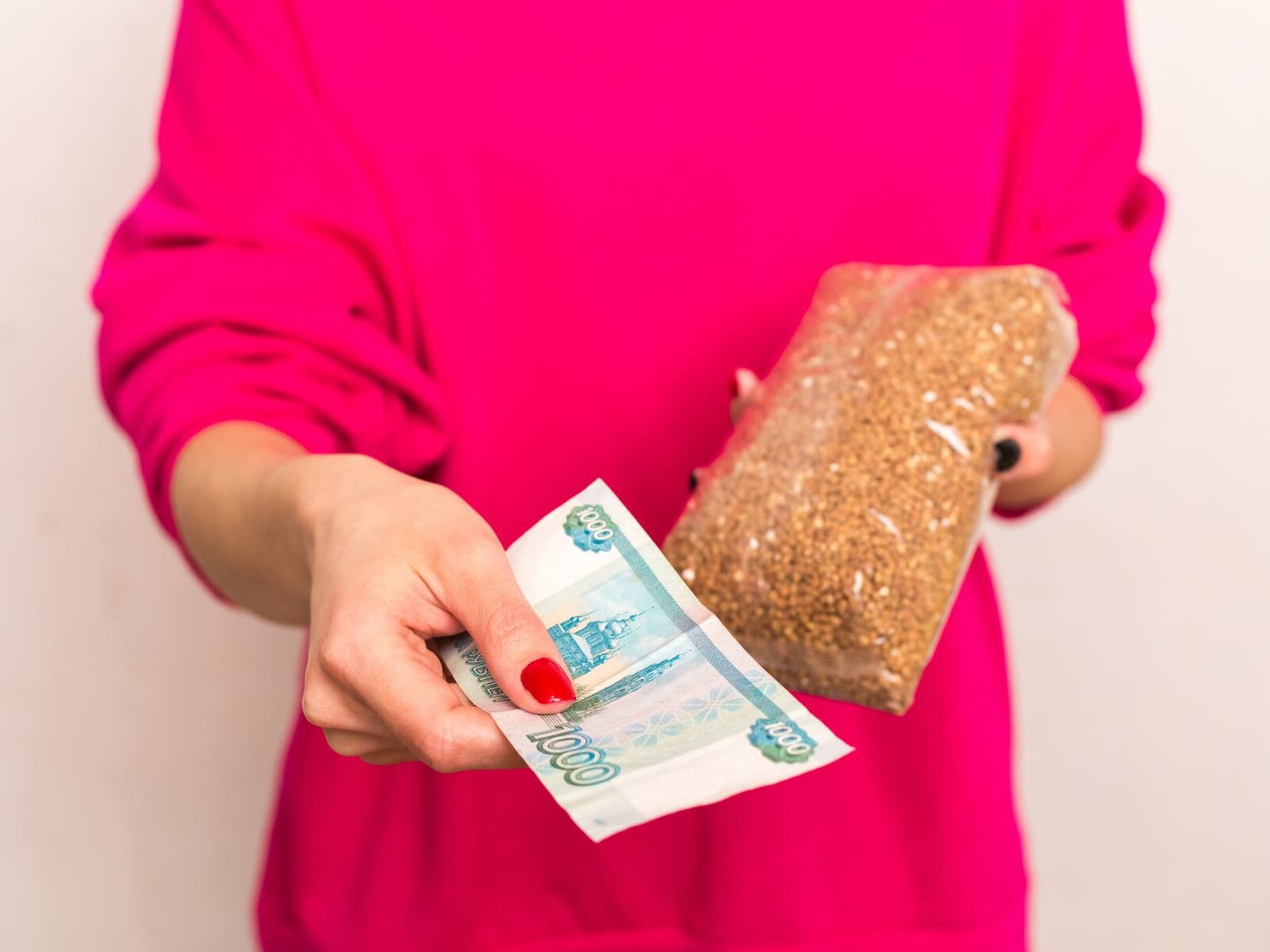 Женщина покупает гречку и протягивает российские рубли.